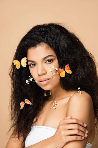 Jovem afro-americana com pequenas flores e borboletas laranja no cabelo isolado no bege — Fotografia de Stock