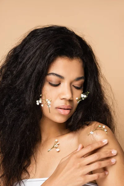 Pretty african american woman with small gypsophila flowers on face and body isolated on beige — Stock Photo