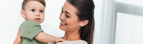 Mujer joven sonriendo mientras sostiene a un niño pequeño, pancarta - foto de stock