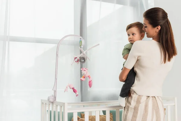 Mamma felice che tiene il bambino vicino al lettino a casa — Foto stock