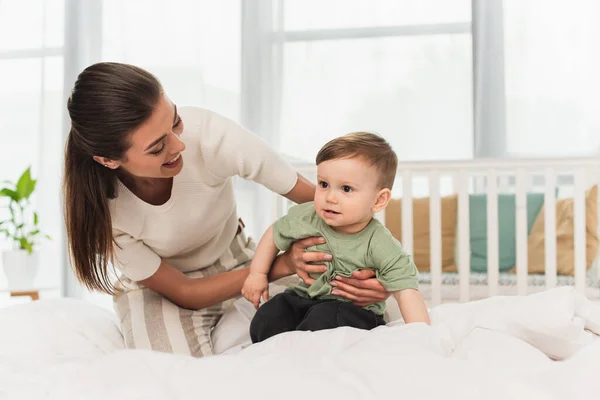 Smiling mother holding toddler kid on bed — Stock Photo