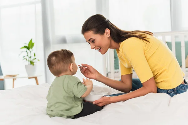 Mãe alegre alimentando filho na cama — Fotografia de Stock