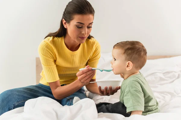 Junge Mutter füttert Kleinkind auf Bett — Stockfoto