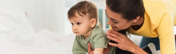 Donna sorridente che tiene il bambino sul letto, striscione — Foto stock