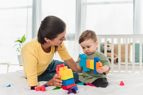 Young woman looking at child playing building blocks on bed — Stock Photo
