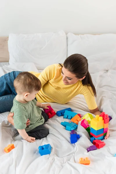 High angle view of smiling mother embracing child with building blocks on bed — Stock Photo
