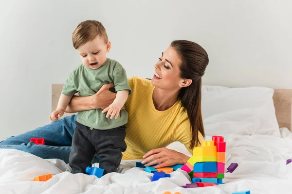 Happy mother embracing toddler son near building blocks on bed — Stock Photo