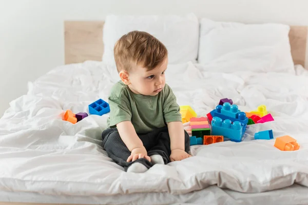 Niño sentado cerca de bloques de construcción en la cama - foto de stock