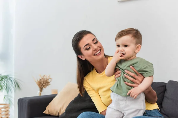 Junge Mutter umarmt fröhlichen Sohn im Wohnzimmer — Stockfoto