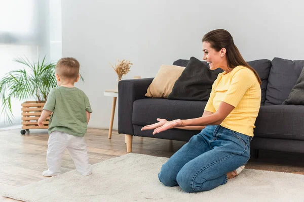 Mère souriante pointant vers l'enfant en bas âge sur le tapis à la maison — Photo de stock