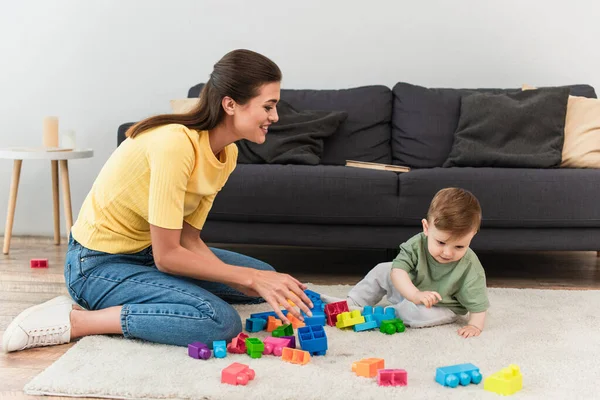 Sorridente madre giocando mattoni in salotto — Foto stock