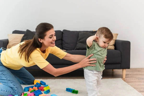 Young mother holding son near colorful building blocks at home — Stock Photo
