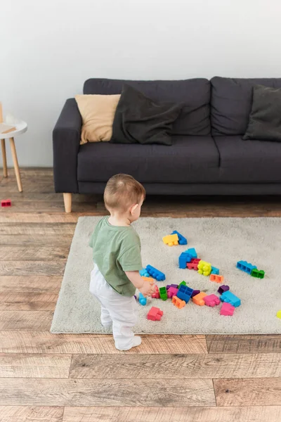 High angle view of toddler boy standing near colorful building blocks at home — Stock Photo