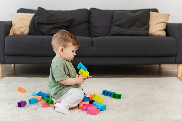 Вид сбоку на мальчика, играющего в строительные блоки на ковре — стоковое фото