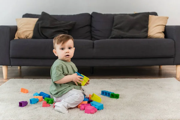 Niño pequeño con bloques de construcción mirando la cámara en la alfombra - foto de stock