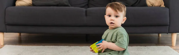 Enfant en bas âge avec des blocs de construction regardant la caméra à la maison, bannière — Photo de stock