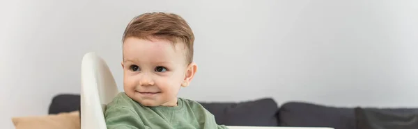 Enfant tout-petit souriant sur une chaise haute à la maison, bannière — Photo de stock