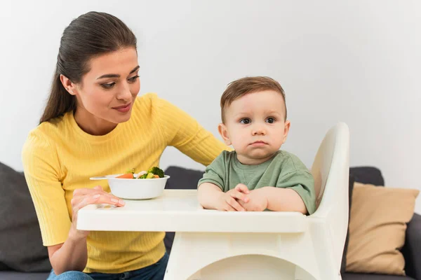 Woman looking at child on high chair near food — Stock Photo