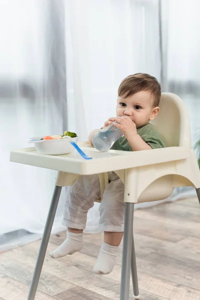 Criança água potável perto de legumes em tigela na cadeira alta — Fotografia de Stock