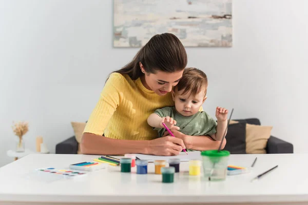 Улыбающаяся мать рисует с маленьким сыном дома — стоковое фото