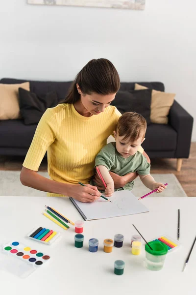 Toddler kid drawing with color pencils near mother and gouache — Stock Photo