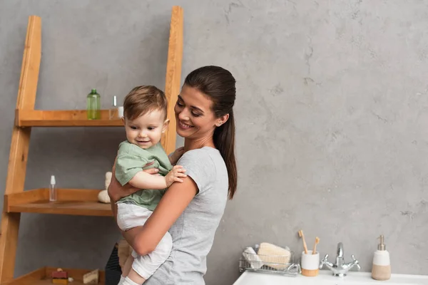 Lächelnde Mutter hält glücklichen Jungen im Badezimmer — Stockfoto