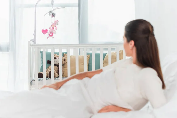Baby crib near blurred woman lying on bed — Stock Photo