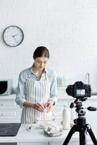 Kulinarik-Bloggerin bricht Hühnerei vor verschwommener Digitalkamera in Schüssel mit Mehl — Stockfoto