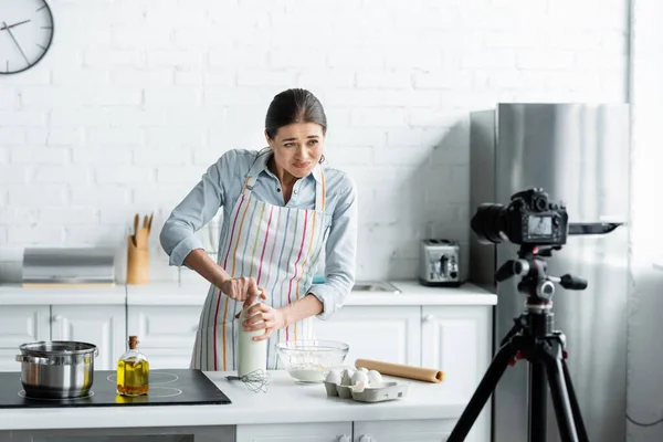 Dona de casa abrindo garrafa de leite na frente câmera digital na cozinha — Fotografia de Stock