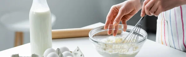 Vue recadrée de la femme mélangeant la pâte dans un bol près du lait et des œufs de poulet, bannière — Photo de stock