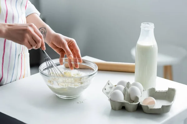 Vista ritagliata della donna che prepara la pasta in ciotola vicino al latte e alle uova di pollo — Foto stock