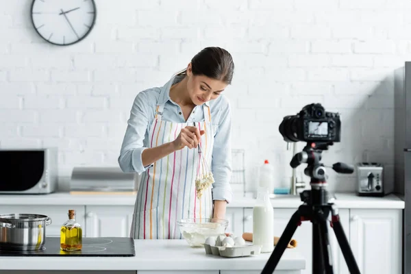 Excited woman preparing dough in front of blurred digital camera — Stock Photo