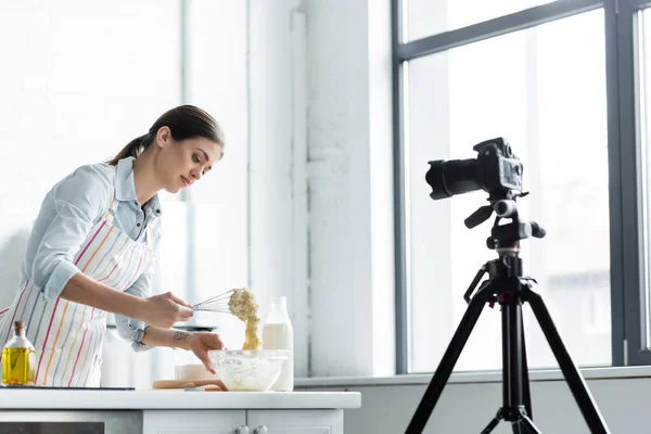 Kulinarische Bloggerin mixt Teig in Schüssel vor Digitalkamera in Küche — Stockfoto