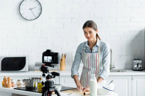 Blogger culinario haciendo masa delante de una cámara digital borrosa en la cocina - foto de stock