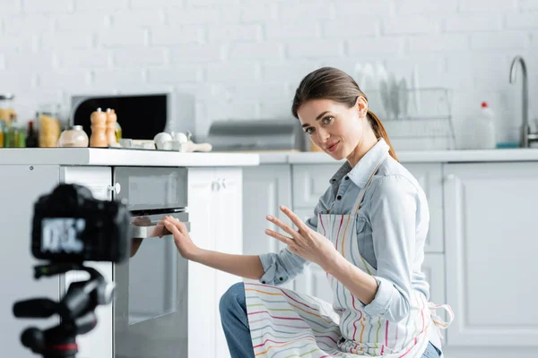 Câmera digital borrada perto de jovem dona de casa mostrando tempo de cozimento perto do forno — Fotografia de Stock