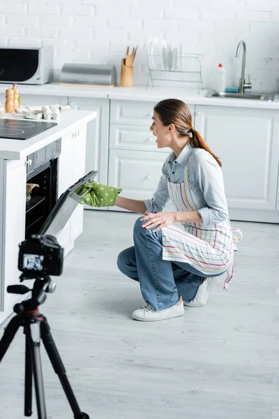 Blogueur culinaire étonnant four d'ouverture près de l'appareil photo numérique flou dans la cuisine — Photo de stock