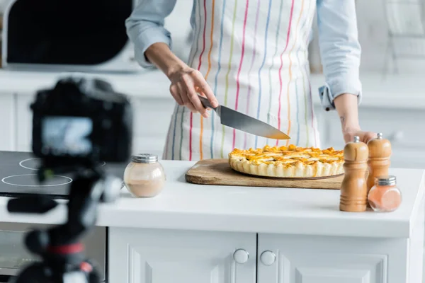 Обрезанный вид кулинарного блогера резки вкусный пирог рядом с размытой цифровой камерой — стоковое фото