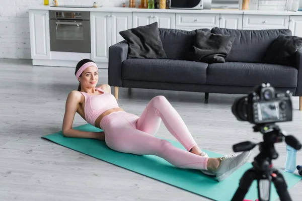 Спортивный блоггер, занимающийся спортом на коврике перед размытой цифровой камерой дома — стоковое фото