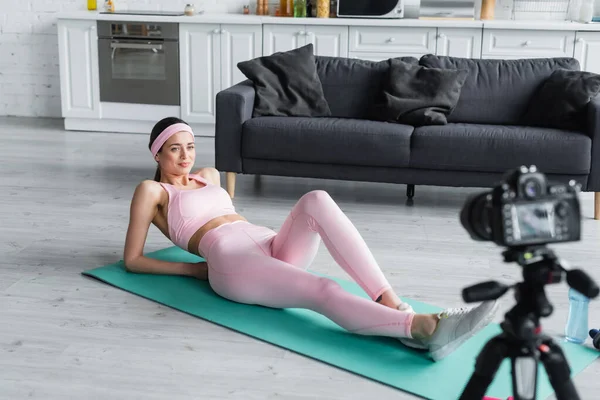 Sports blogger exercising on fitness mat in front of blurred digital camera at home — Stock Photo