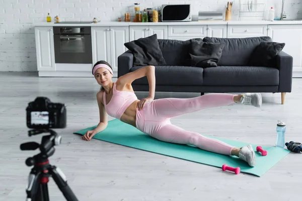 Young sportswoman exercising on fitness mat in front of blurred digital camera — Stock Photo