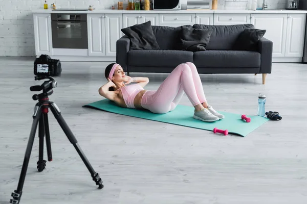 Mujer deportiva haciendo ejercicio abdominales cerca de pesas, botella deportiva y cámara digital - foto de stock