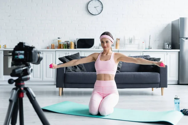 Treinamento esportivo mulher com halteres perto de câmera digital borrada em casa — Fotografia de Stock