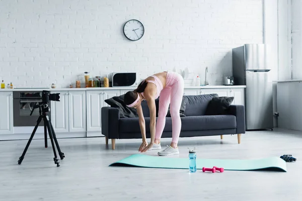 Sportswoman doing forward bend exercise near digital camera in modern kitchen — Stock Photo