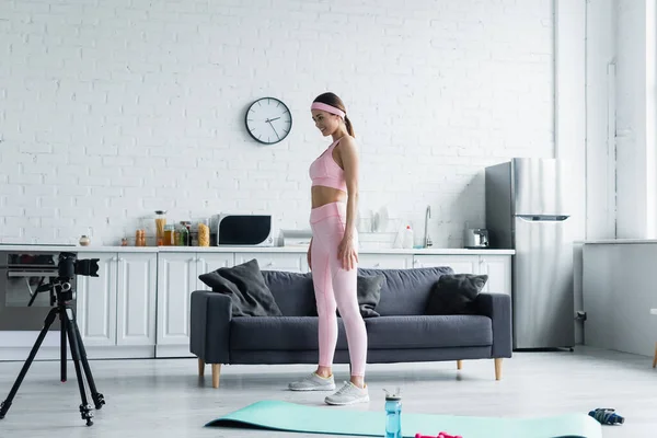 Vue pleine longueur de la femme sportive debout près de l'appareil photo numérique sur trépied dans la cuisine — Photo de stock