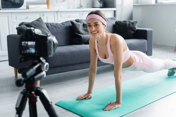 Happy sports blogger training in plank pose in front of blurred digital camera — Stock Photo