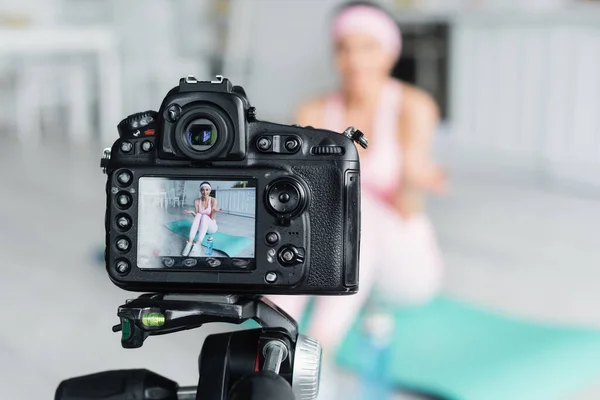 Selective focus of digital camera near sports blogger talking on fitness mat — Stock Photo