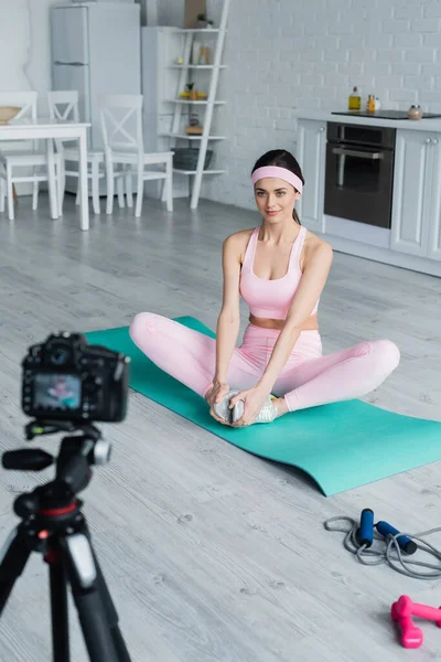 Joli sport blogueur formation sur tapis de fitness près flou appareil photo numérique — Photo de stock