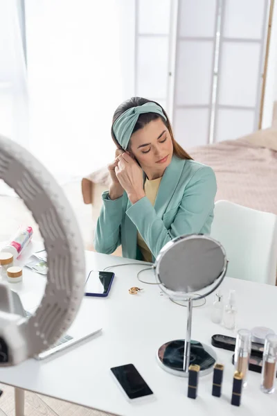 Joven blogger de belleza preparándose para grabar cerca del titular del teléfono y contenedores con cosméticos - foto de stock