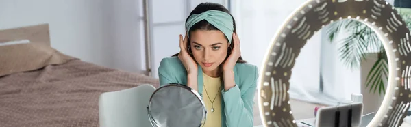 Stylish beauty blogger adjusting headband while preparing to video record near phone holder, banner — Stock Photo