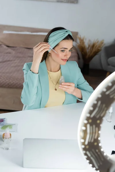 Блогер красоты применяет сыворотку для лица рядом с ноутбуком и кругом света — стоковое фото